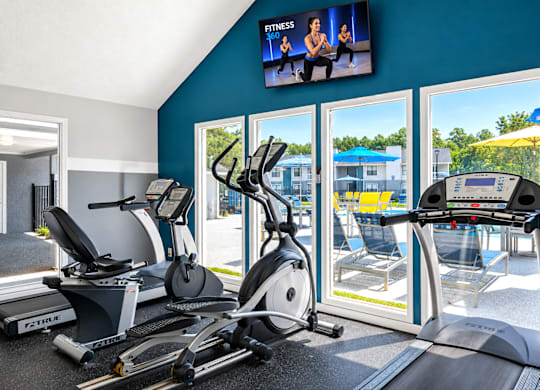 A fitness room with treadmills, elliptical machines, and a television showing a fitness program.
