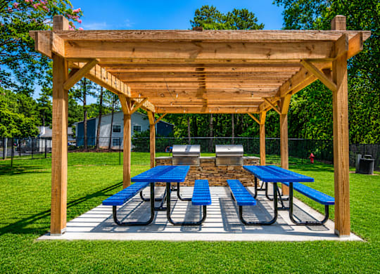 A wooden pergola with blue benches is set up in a grassy area.