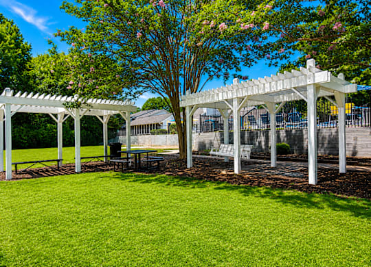A white pergola with a table and chairs underneath it.