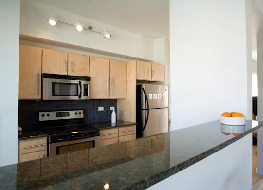 A modern kitchen with a black countertop and stainless steel appliances.