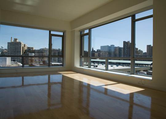 A room with a wooden floor and large windows overlooking a cityscape.