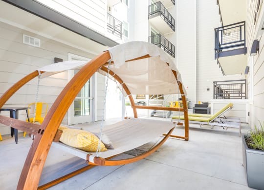 a hammock chair with a yellow pillow sits on a patio in front of a white building