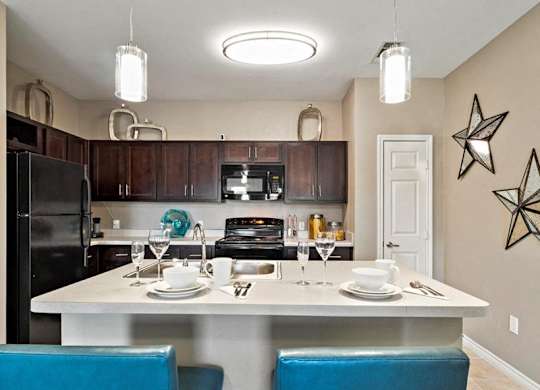 A kitchen with a table set for two and a black refrigerator.