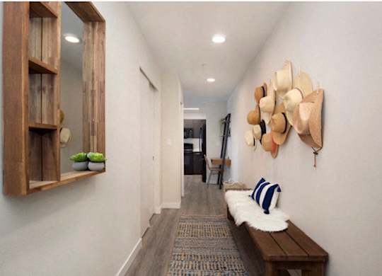 Hallway with plank flooring, mirror,  and storage bench with hats haning on the wall for artsy decoration at Arabella Apartment Homes, Washington, 98155