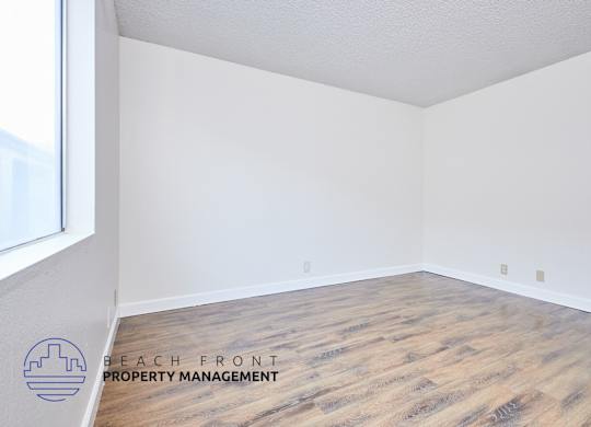 A room with wooden flooring and a logo for Beach Front Property Management.