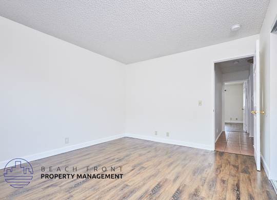 A room with wooden floors and white walls, with a doorway leading to another room.