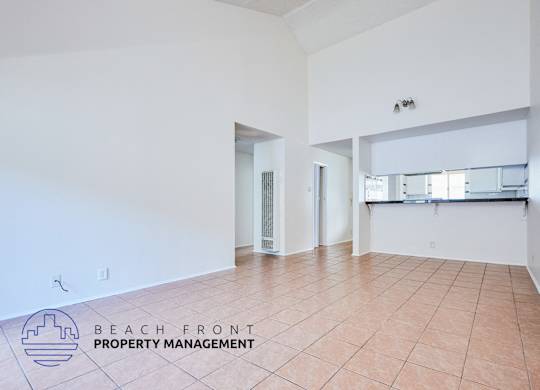 A spacious room with tiled flooring and white walls, with a logo for Beach Front Property Management in the bottom left corner.
