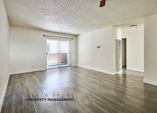 A spacious room with wooden floors and a sliding glass door leading to a balcony.
