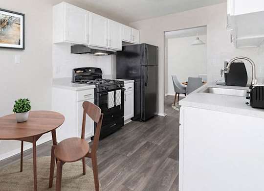 apartment kitchen with white cabinets, black appliances, gray plank flooring and a small table