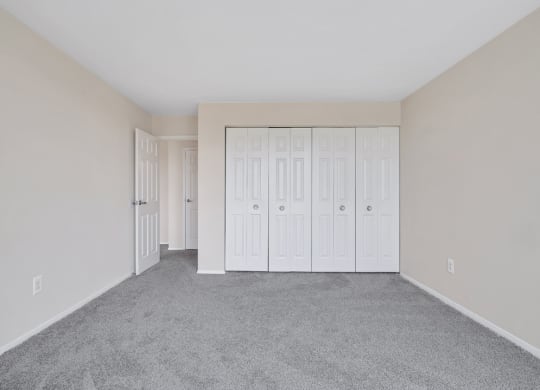 an empty bedroom with white closets and carpeting