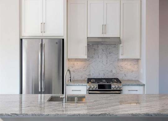 A kitchen with a marble backsplash and a stainless steel refrigerator.