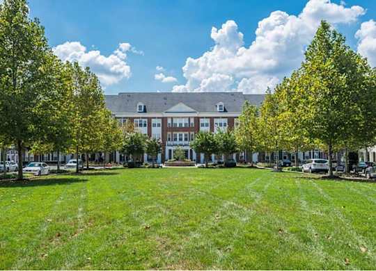 A large building with a red brick facade is surrounded by a grassy area with trees.