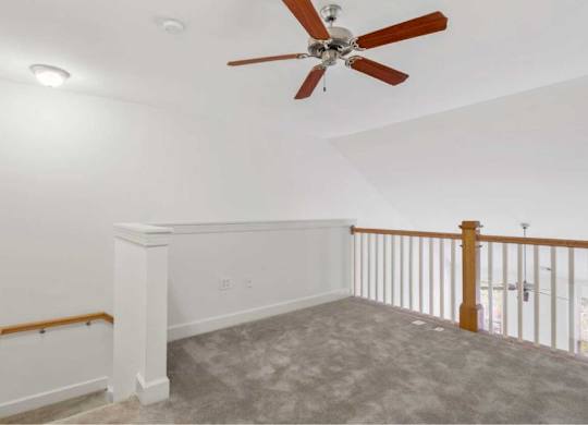 an empty living room with a ceiling fan and a staircase
