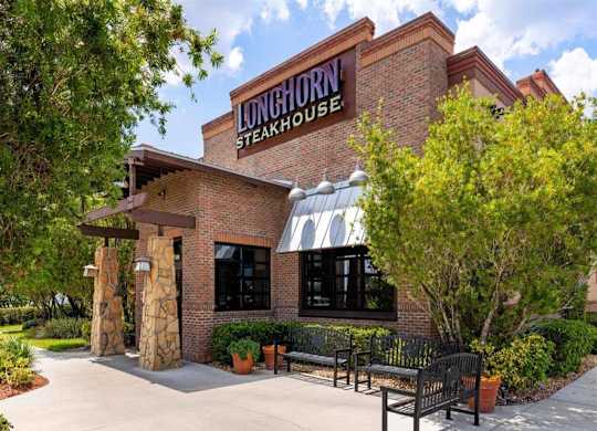 the exterior of the longhorn steakhouse with benches and trees