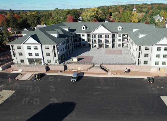 A large white building with a green roof is surrounded by a parking lot.