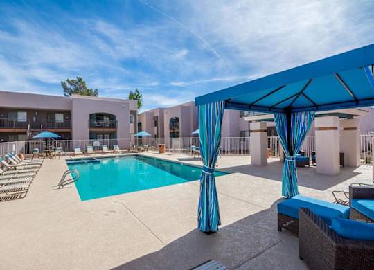 A pool area with a blue canopy and lounge chairs.
