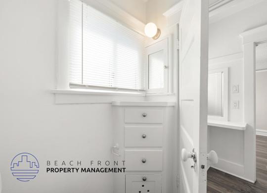 A white room with a dresser and a mirror with a logo of Beach Front Property Management.