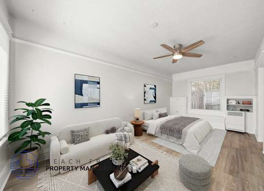 A well-lit, spacious living room with a white sofa, a grey ottoman, and a coffee table.