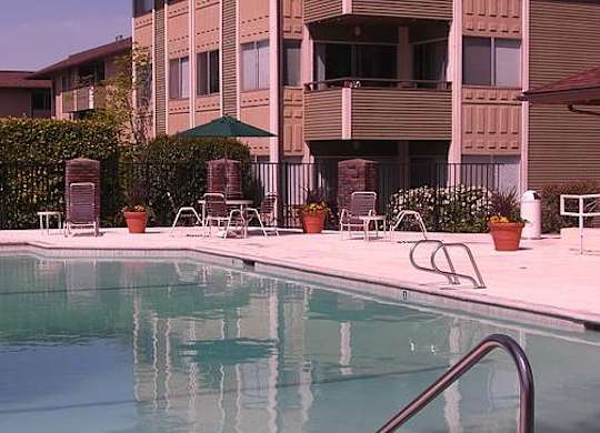 A pool in front of a building with a green umbrella.