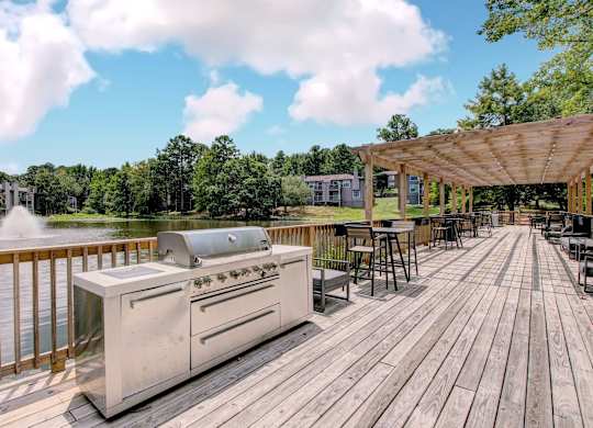 A grill is on a wooden deck next to a body of water.