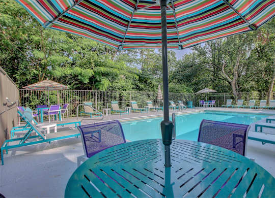 A colorful striped umbrella shades a table and chairs by a pool.