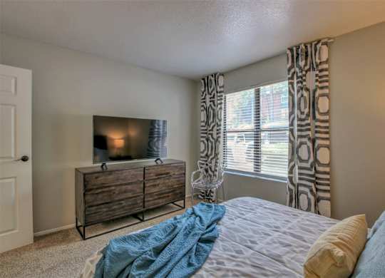A bedroom with a bed, a dresser, and a window with curtains.