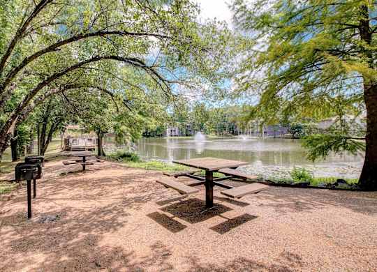 A picnic table is in the middle of a dirt area with a mailbox to the left and a tree to the right.