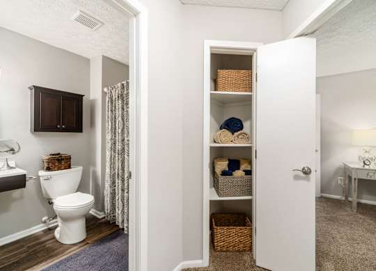 A white bathroom with a toilet, a cabinet, a towel, and a basket.