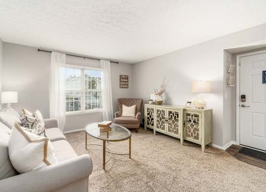 A living room with a white couch, a coffee table, and a window with curtains.