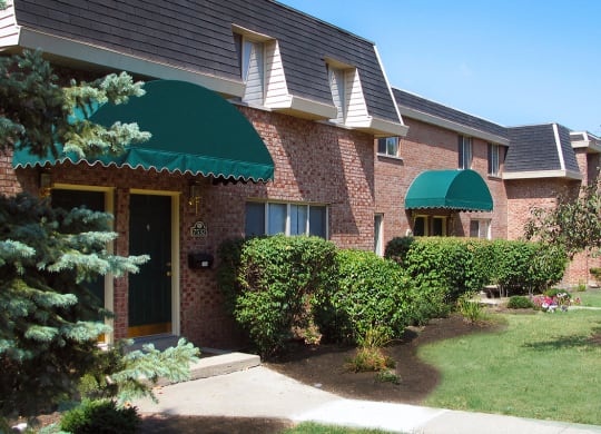a brick house with a green awning and bushes in front of it at Wentworth Estates Apartments, Kentucky