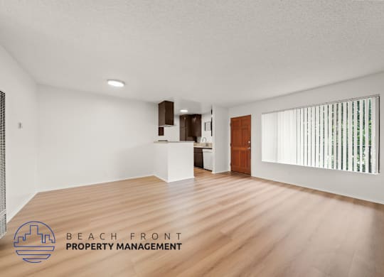 A spacious room with wooden flooring and a logo for Beach Front Property Management in the corner.