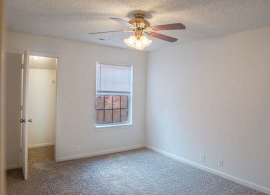 A room with a ceiling fan and a window with a view of a building outside.