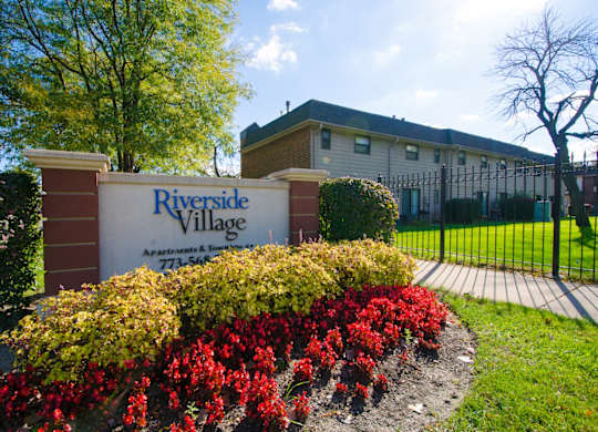A sign for Riverside Village Apartments stands in front of a building.