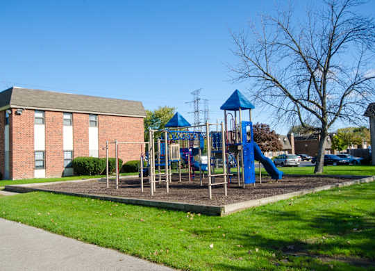 A playground with a blue slide and a red building in the background.