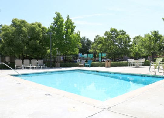 a swimming pool with lounge chairs and trees in the background