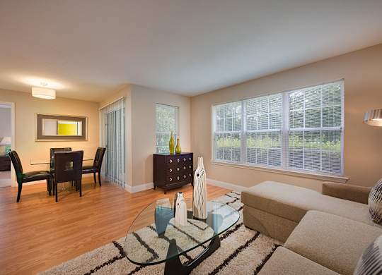 Furnished apartment living room showing abundant windows, balcony, and dining area in the background.
