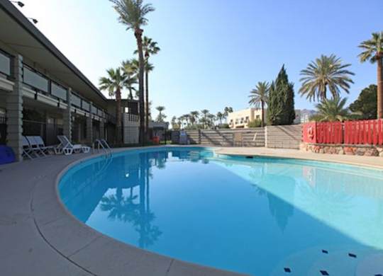 A swimming pool with a blue tinted water and white lounge chairs.