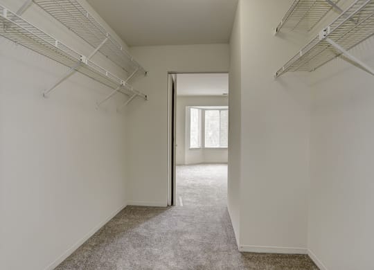 a walk in closet in a bedroom with white walls and a door to a room