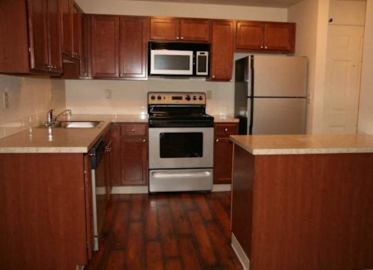 a kitchen with brown wooden cabinets and stainless steel appliances at Heritage Grove Apartments in Renton, WA