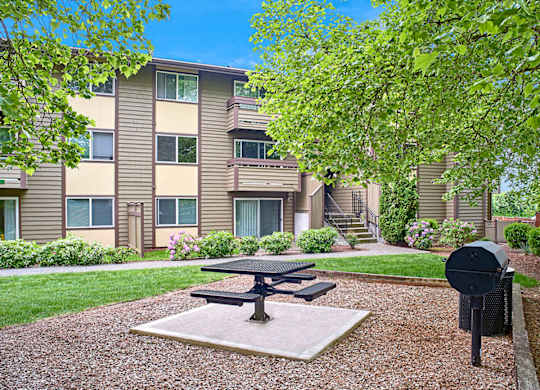 Exterior view of patio area and BBQ, manicured grounds and building, and blue skies in the background at Heritage Grove, Renton, WA.