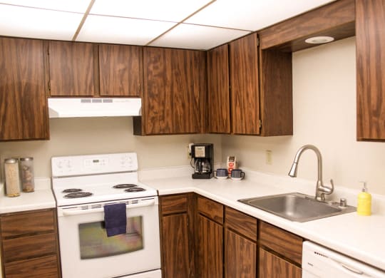 L shaped kitchen with brown cabinets, white appliances and stainless steel sink.
