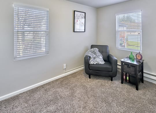 Carpeted living space, with two windows on two walls. Staged with a chair and side table.at Woodhaven, Everett, WA 98203