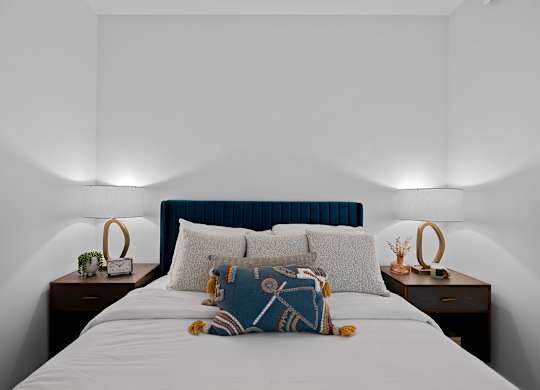 A bed with a blue headboard and a white comforter with a pillow and a teddy bear on it.