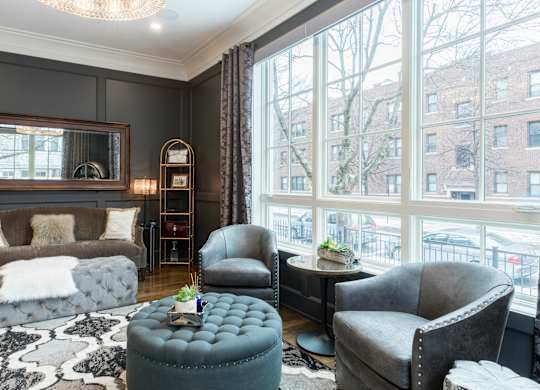 A living room with a grey couch, a grey armchair, a grey ottoman, and a black and white rug.