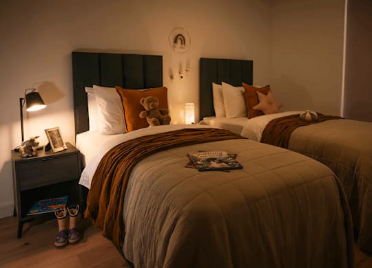 Two beds with pillows and a lamp on a nightstand. at Cherrywood Apartments, D18 VY3V