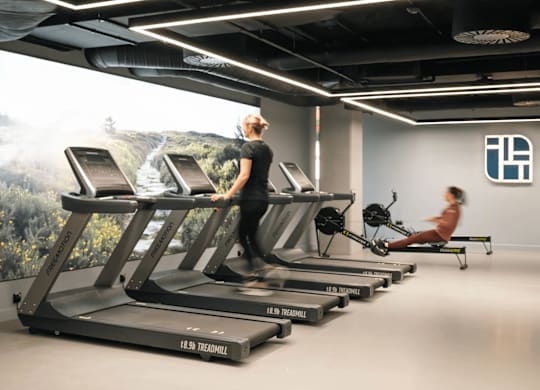 A woman is running on a treadmill in a gym with a wall mural of a forest. at Cherrywood Apartments, D18 VY3V, DUBLIN 18