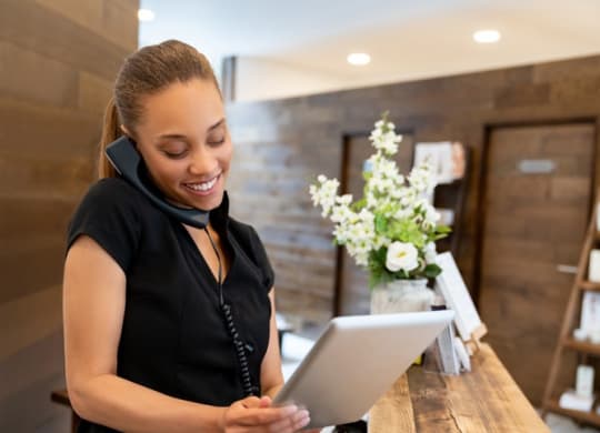 A woman in a black shirt is talking on the phone and using a tablet.