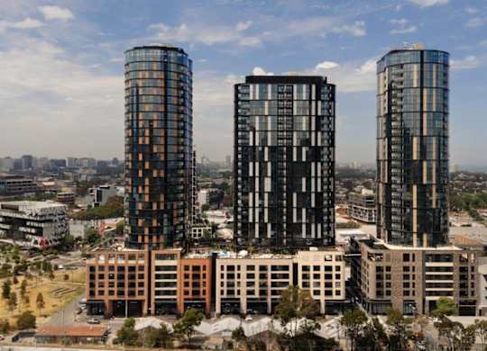 Three tall buildings with glass windows are in the foreground of a cityscape.