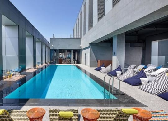 A modern pool area with a long rectangular pool surrounded by lounge chairs and tables.