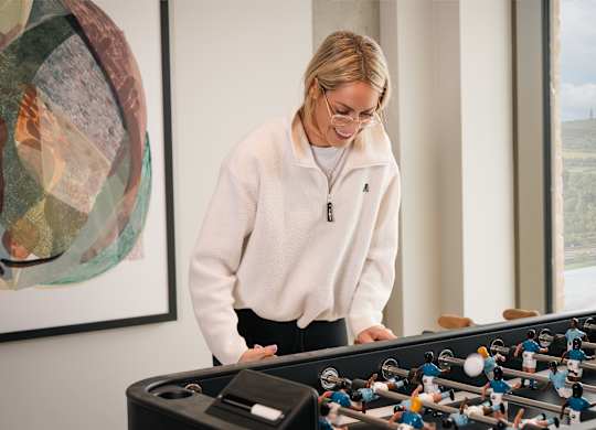 A woman playing a foosball table in a room with a painting on the wall at Cherrywood Apartments, D18 VY3V